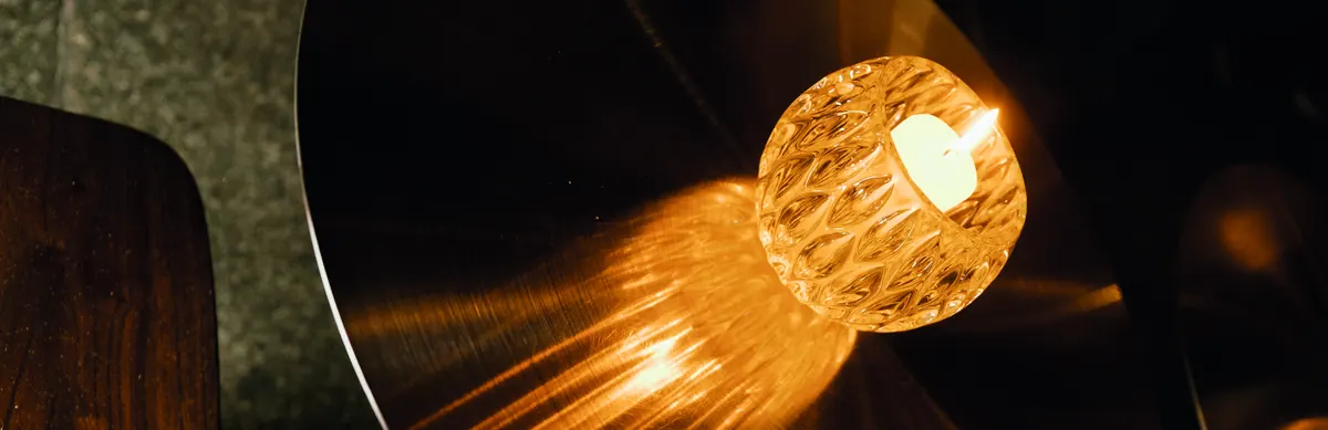 A crystal votive throwing amber light across a dark table.