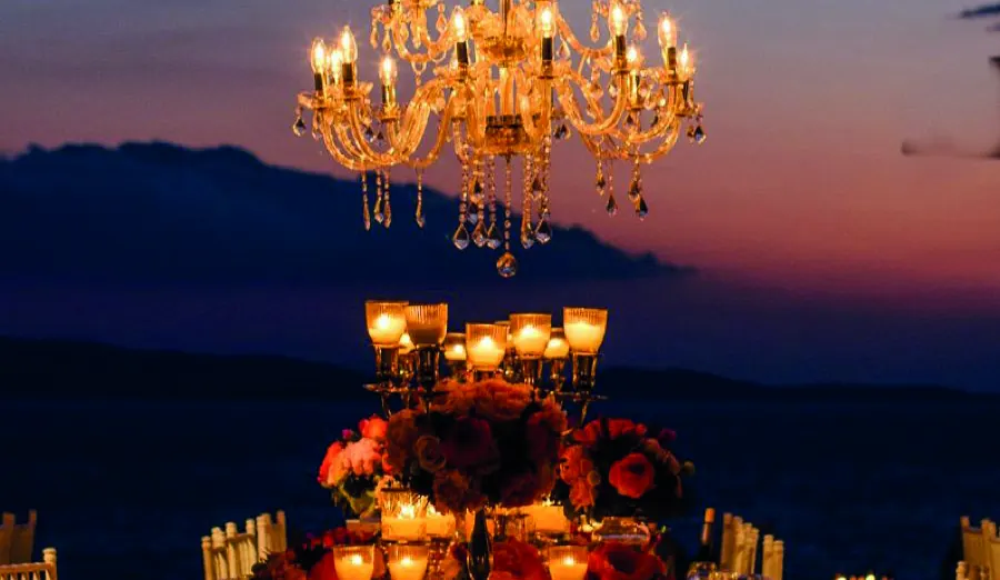 A crystal chandelier above a candlelit table at dusk, by the sea.