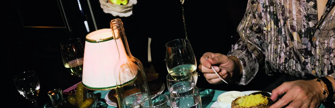 A night table seen from above: lamp, glasses and the hands of the guests.