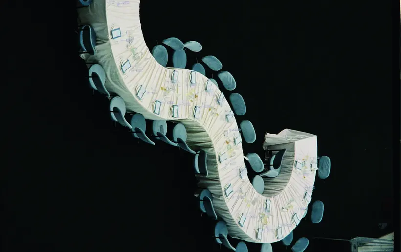 A serpentine table seen from above, its pale blue chairs set against black.